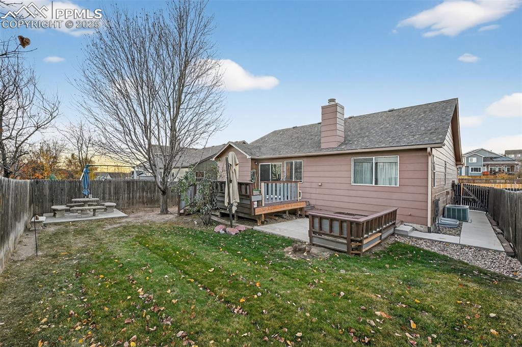 Rear view of property with a fenced backyard, a wooden deck, a patio, and a chimney