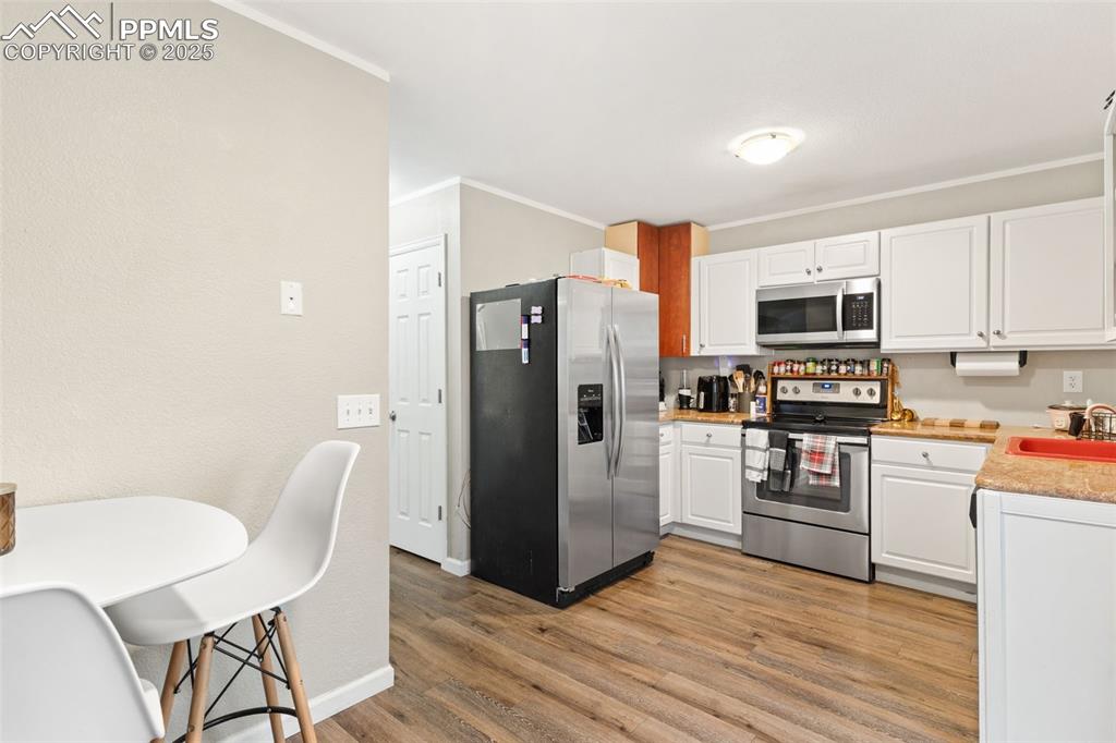 Kitchen featuring appliances with stainless steel finishes, white cabinets, light wood-type flooring, and ornamental molding