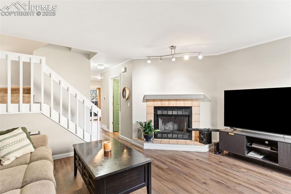 Living room featuring stairway, a tiled fireplace, wood finished floors, and ornamental molding