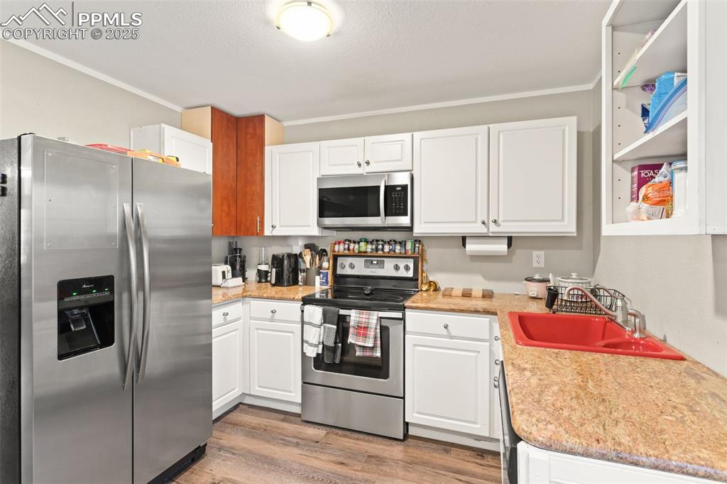 Kitchen featuring appliances with stainless steel finishes, white cabinetry, light wood-style flooring, crown molding, and light stone counters