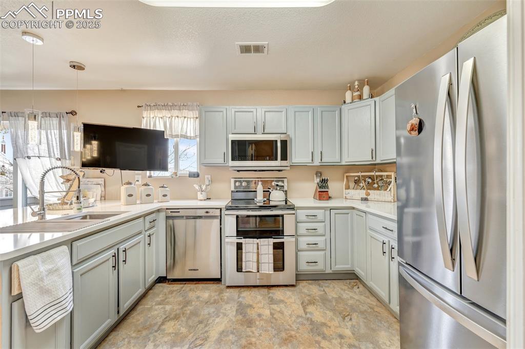 Kitchen with visible vents, a sink, light countertops, stainless steel appliances, and stone finish flooring