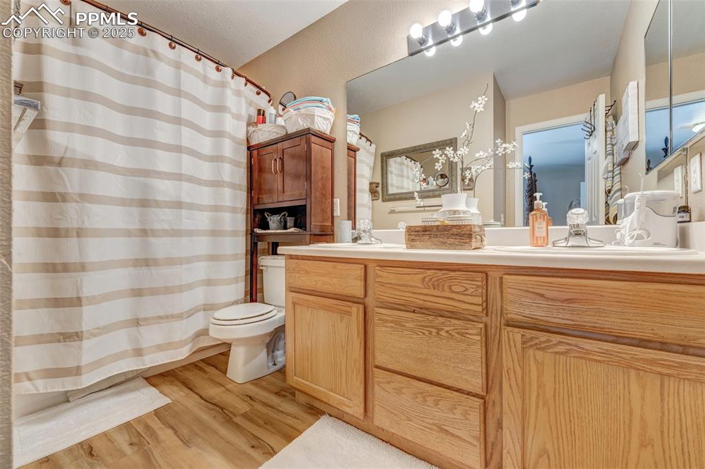 Full bath featuring a sink, double vanity, toilet, and wood finished floors