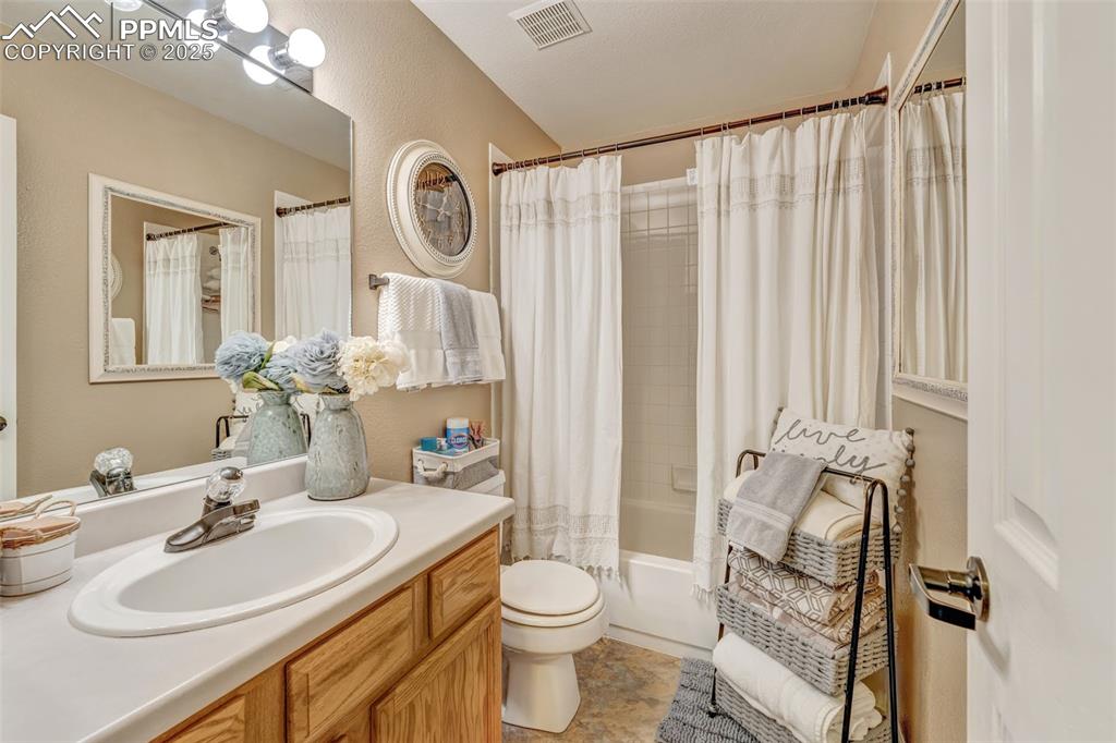Full bath with toilet, vanity, shower / tub combo with curtain, and visible vents