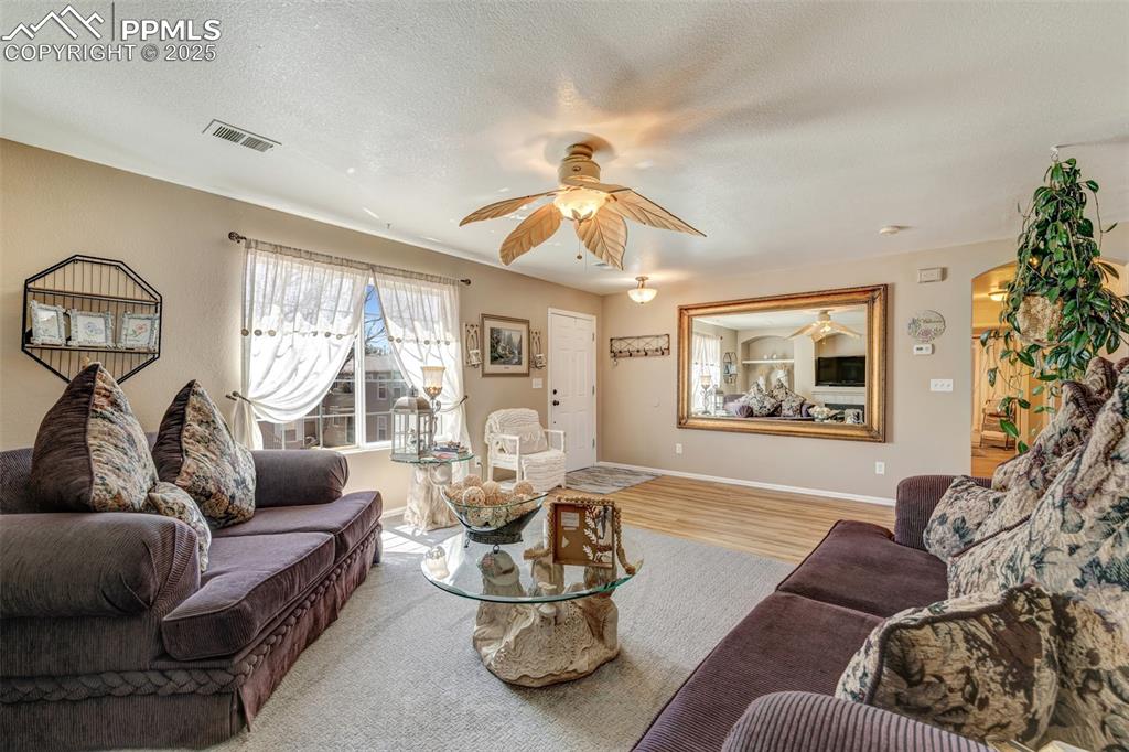 Living area featuring baseboards, a textured ceiling, visible vents, ceiling fan, and wood finished floors