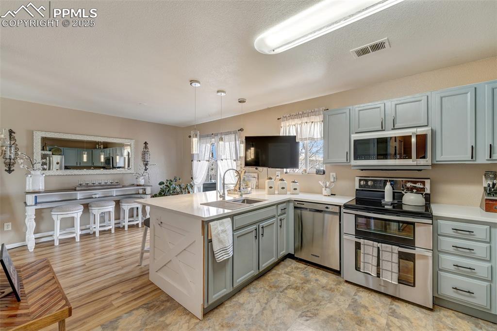 Kitchen with visible vents, a sink, light countertops, appliances with stainless steel finishes, and a peninsula