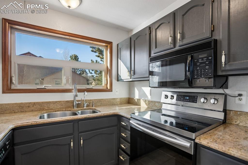 Kitchen featuring black appliances, light stone countertops, and gray cabinets