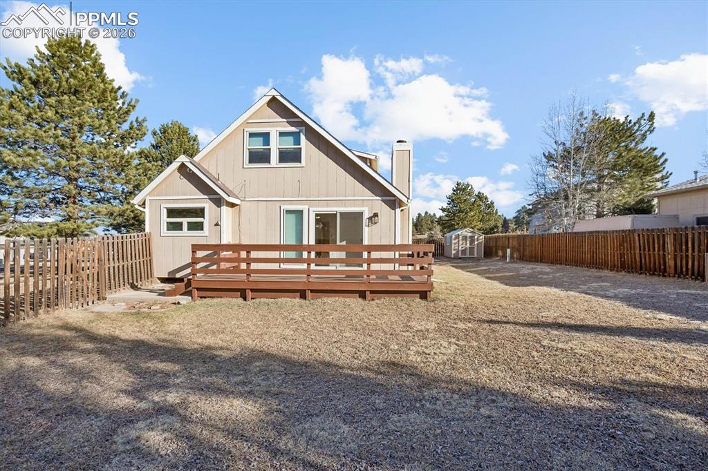 Rear view of house featuring a wooden deck, a fenced backyard, a shed, and a chimney