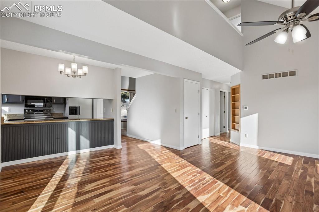 Unfurnished living room with built in features, dark wood-style flooring, a high ceiling, a ceiling fan, and a chandelier