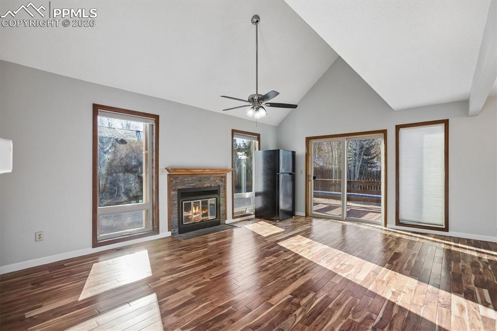 Unfurnished living room featuring vaulted ceiling, dark wood-style flooring, a ceiling fan, and a fireplace with flush hearth