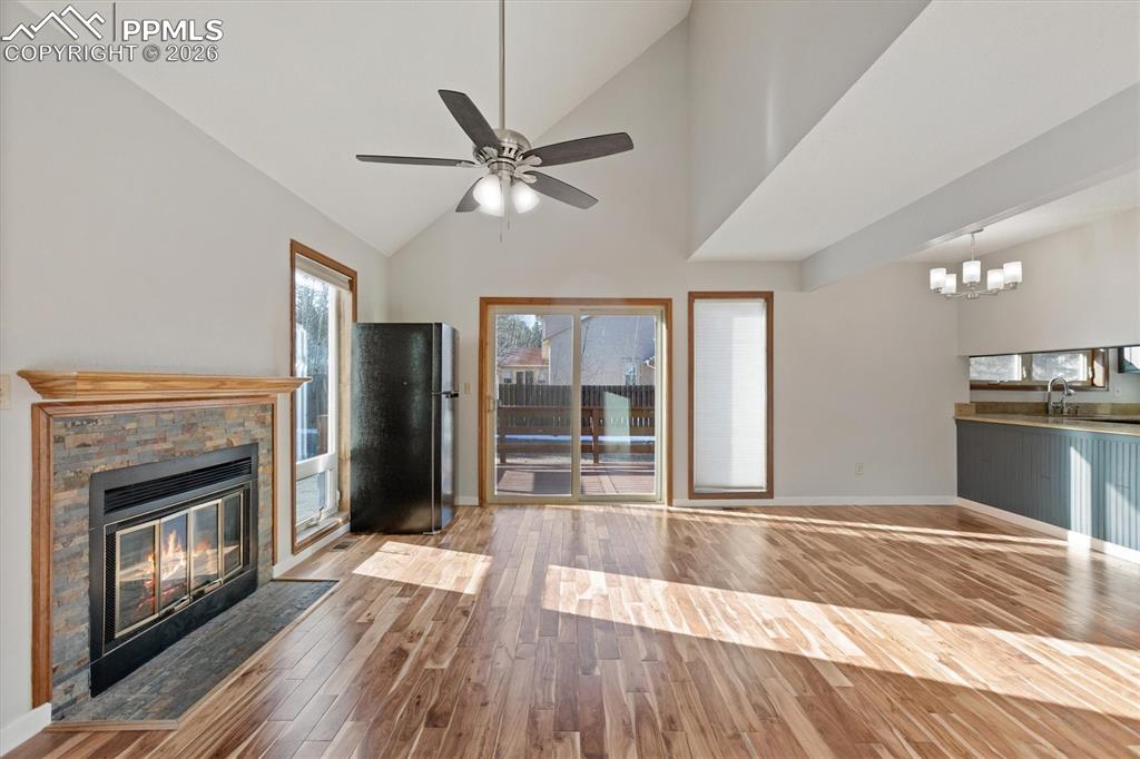 Unfurnished living room with lofted ceiling, wood finished floors, ceiling fan, a fireplace, and hanging lights