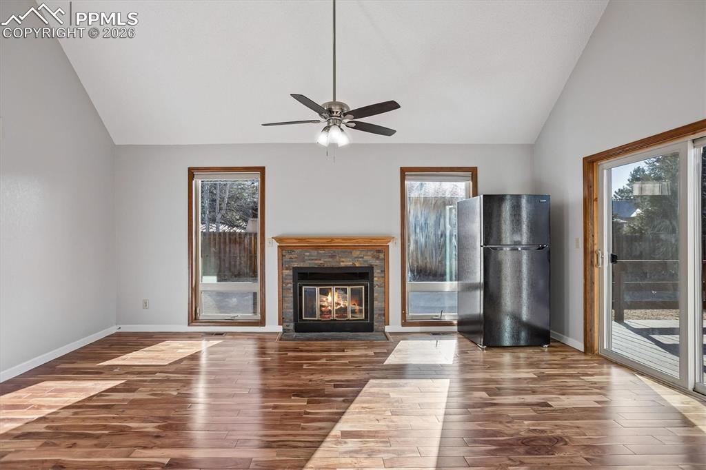 Unfurnished living room with lofted ceiling, hardwood / wood-style flooring, ceiling fan, and a brick fireplace
