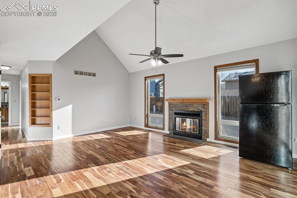 Unfurnished living room featuring built in shelves, wood-type flooring, vaulted ceiling, healthy amount of natural light, and a stone fireplace