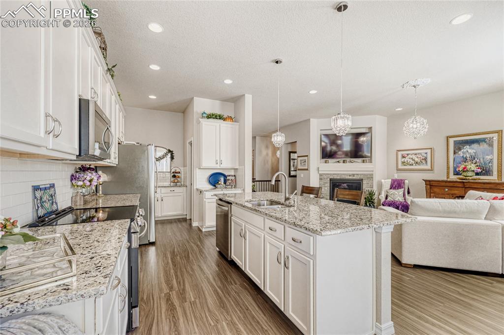 Kitchen featuring stainless steel appliances, open floor plan, white cabinets, a glass covered fireplace, and a center island with sink