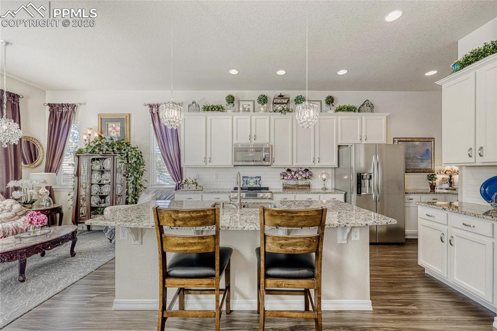 Kitchen with hanging lights, stainless steel appliances, a kitchen island with sink, white cabinets, and a textured ceiling
