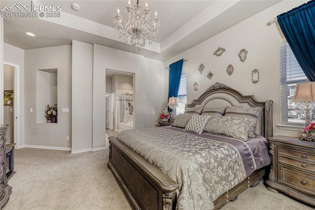 Bedroom featuring a tray ceiling, ensuite bath, light carpet, and suspended lighting