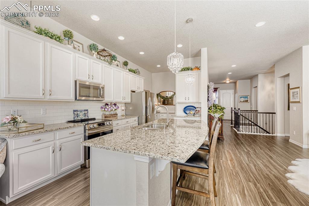 Kitchen with white cabinetry, stainless steel appliances, a breakfast bar, light wood-type flooring, and a textured ceiling