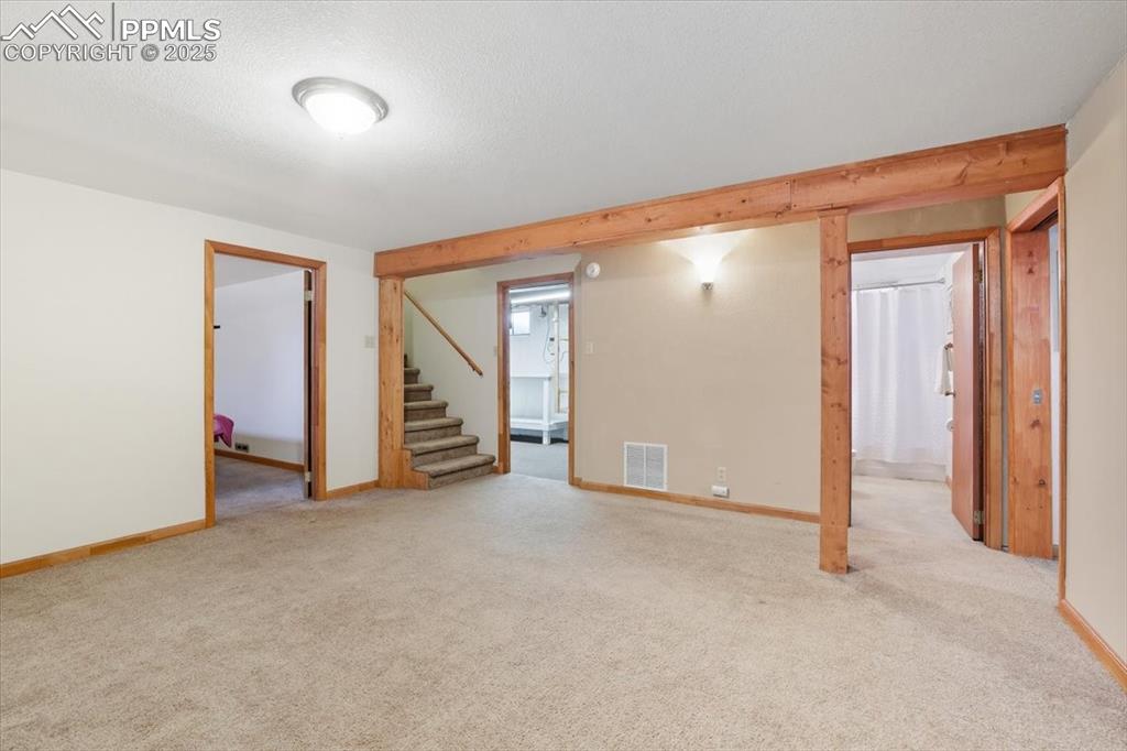 Empty room with stairs, light colored carpet, and a textured ceiling
