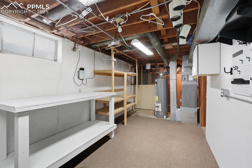 Unfinished basement featuring light carpet, gas water heater, and heating unit