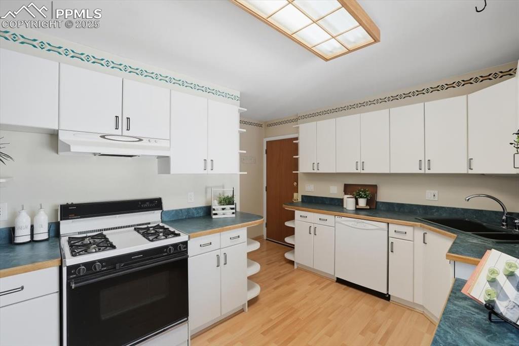 Kitchen with gas range, open shelves, dishwasher, light wood finished floors, and white cabinets