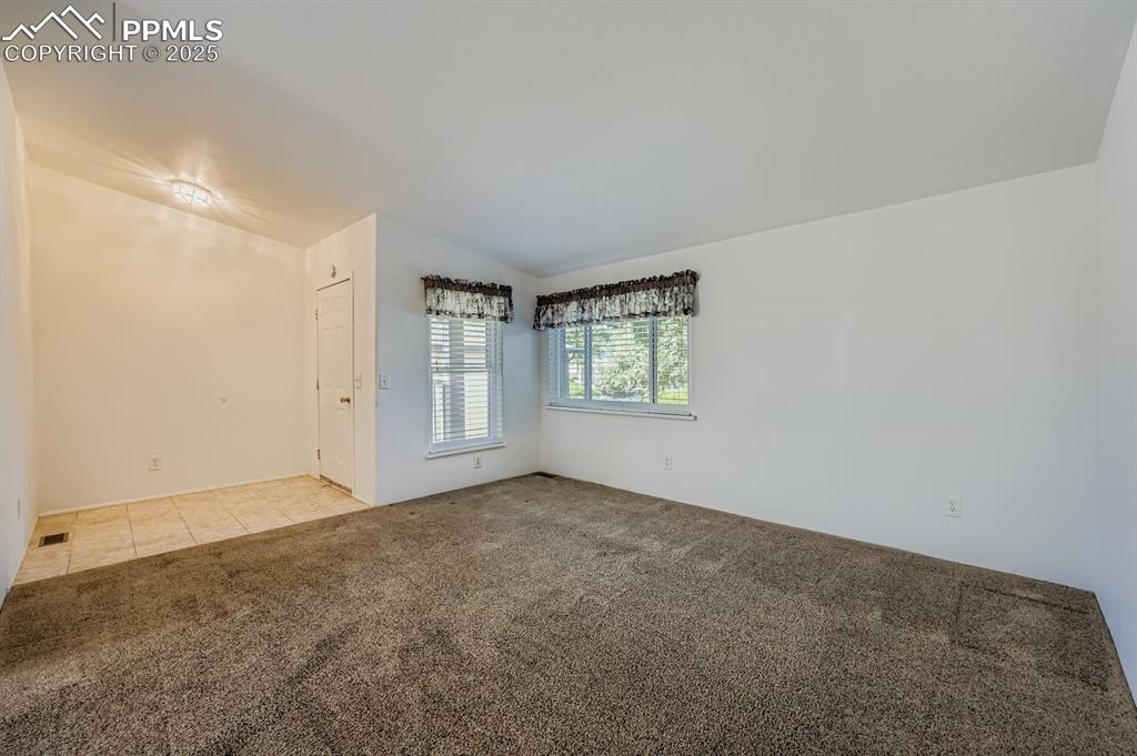 Spare room featuring light colored carpet, lofted ceiling, and light tile patterned floors