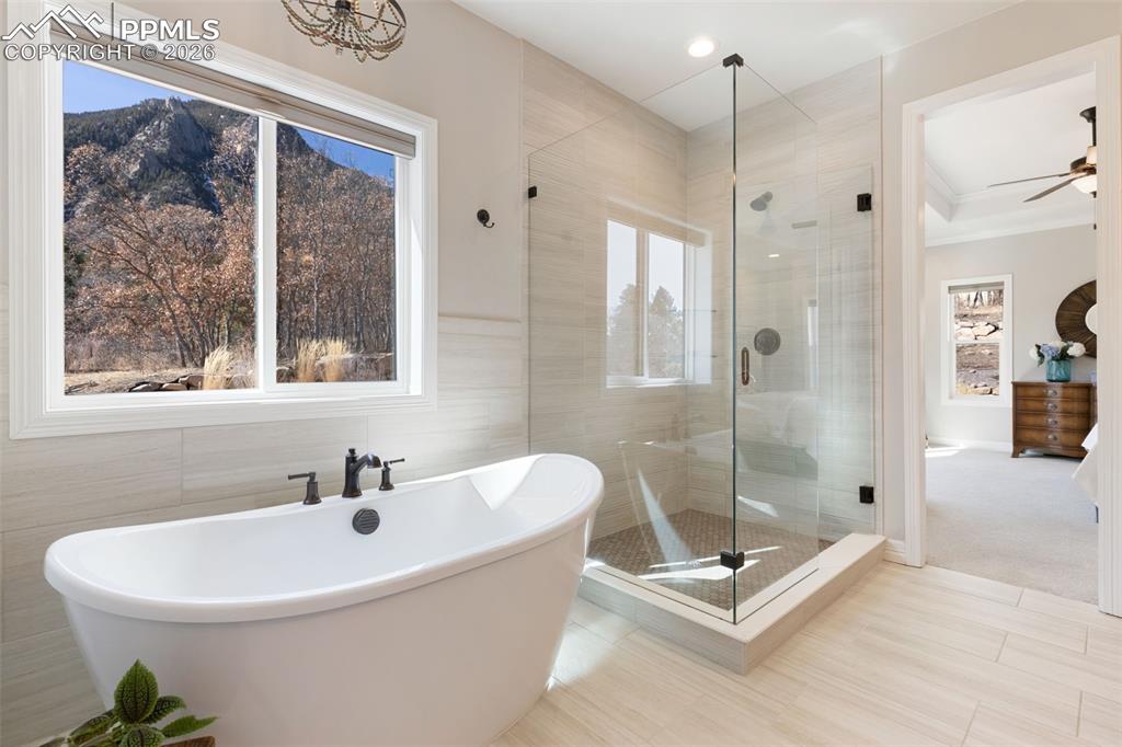 A freestanding soaking tub is positioned beneath a large picture window, offering a secluded, spa-like escape with direct views of the rugged mountain peaks
