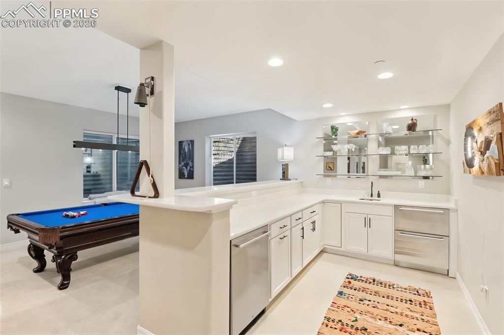 The fully equipped wet bar, complete with a dishwasher, beverage center, and glass display shelving, serves the entertainment area effortlessly.
