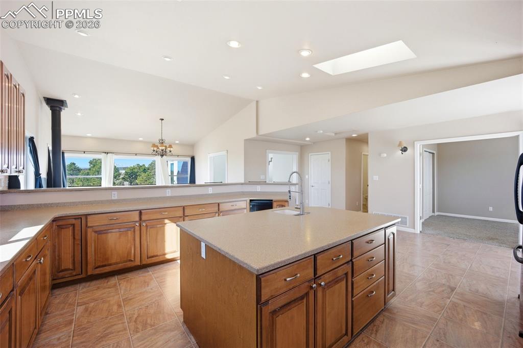 Kitchen featuring wood finish cabinetry, lofted ceiling, a center island with sink, and 2 skylights