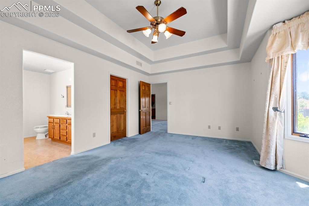 Unfurnished bedroom featuring a tray ceiling, carpet, a ceiling fan, connected bathroom, and a closet