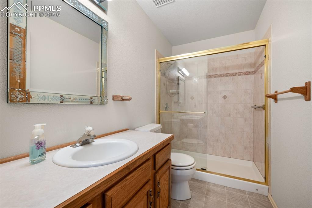 Full bath featuring vanity, a shower stall, light tile patterned floors, and a textured wall