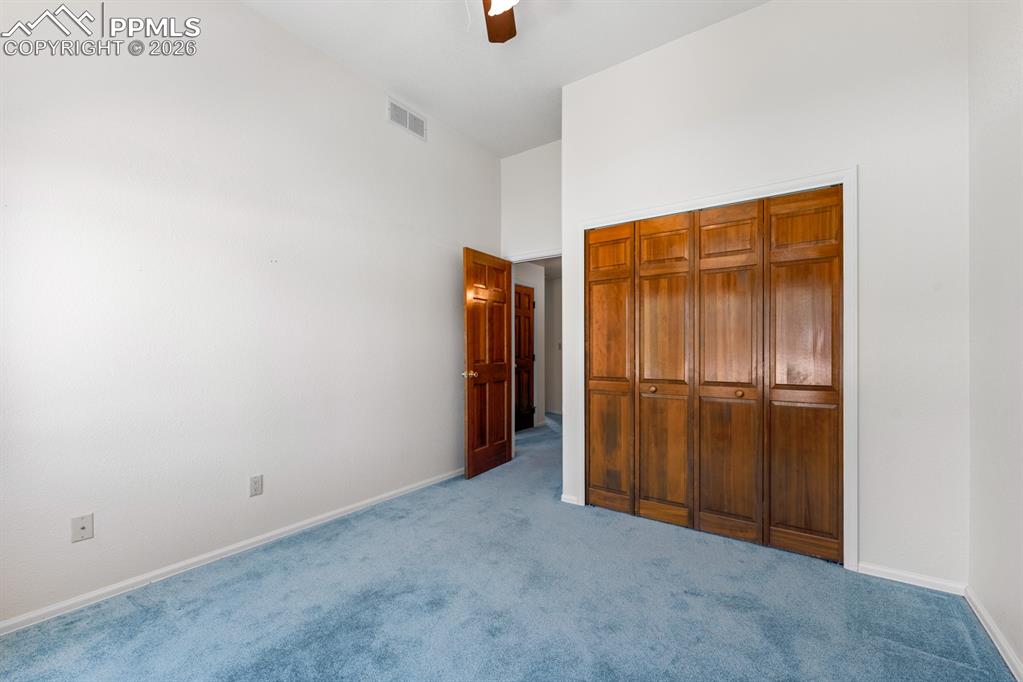 Unfurnished bedroom with carpet floors, ceiling fan, a closet, and a high ceiling