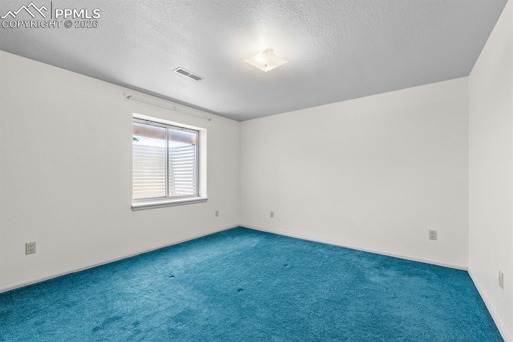 Carpeted spare room featuring a textured ceiling and baseboards
