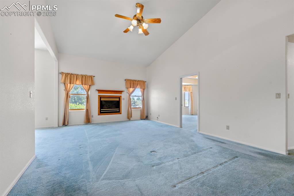 Unfurnished living room with a glass covered fireplace, light colored carpet, a ceiling fan, and lofted ceiling