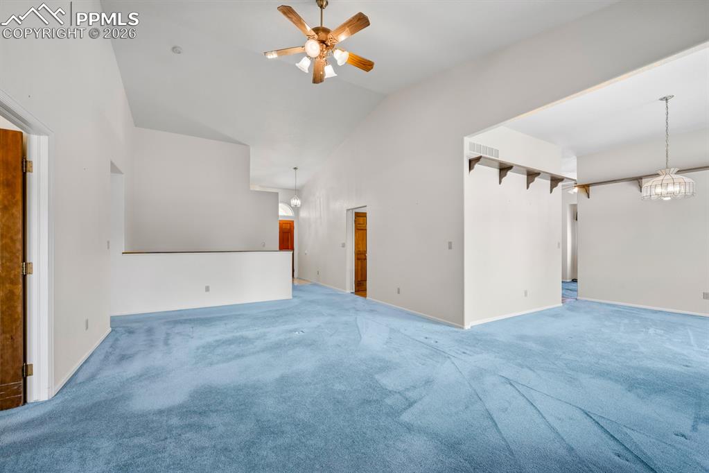 Unfurnished living room featuring carpet, a ceiling fan, a chandelier, and vaulted ceiling