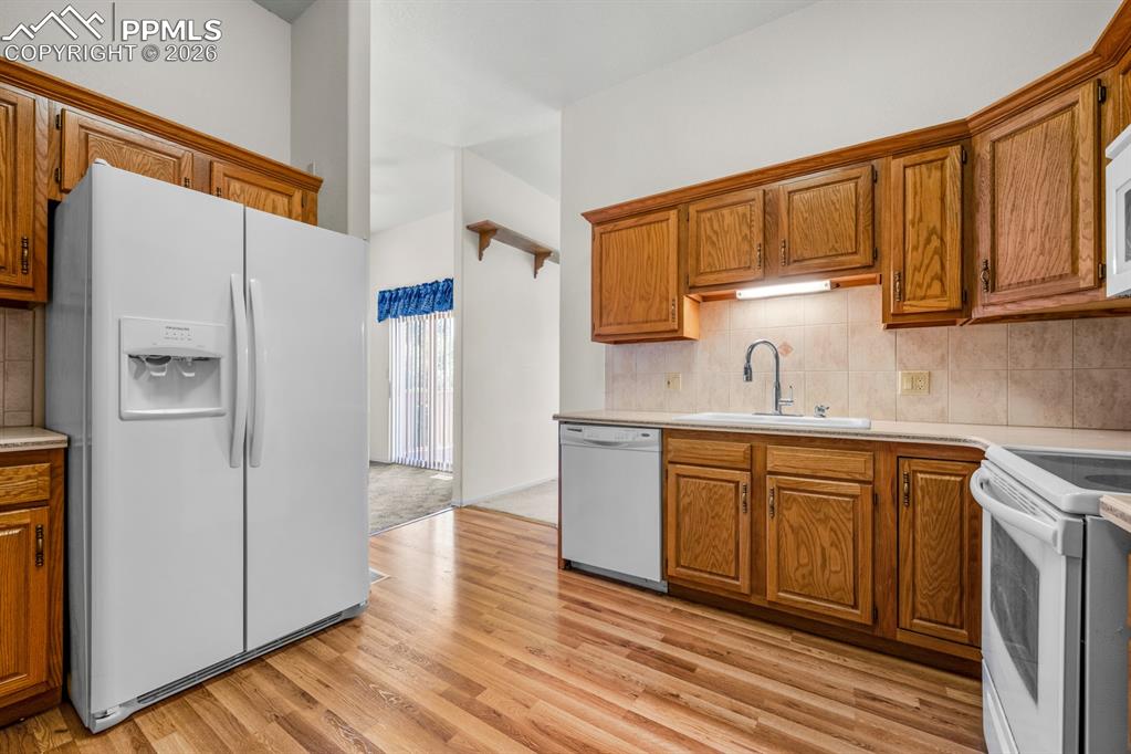 Kitchen featuring white appliances, light countertops, wood finish cabinets, and backsplash