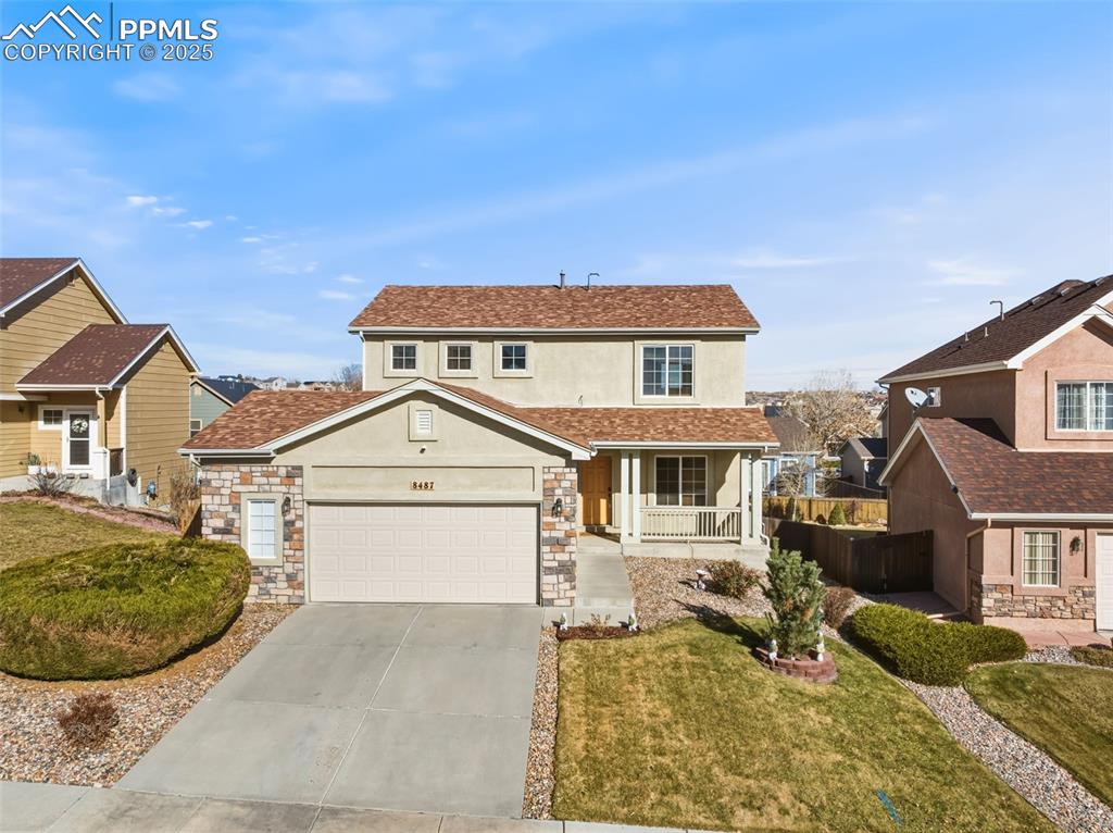 Traditional home with stucco siding, a porch, concrete driveway, stone siding, and a shingled roof