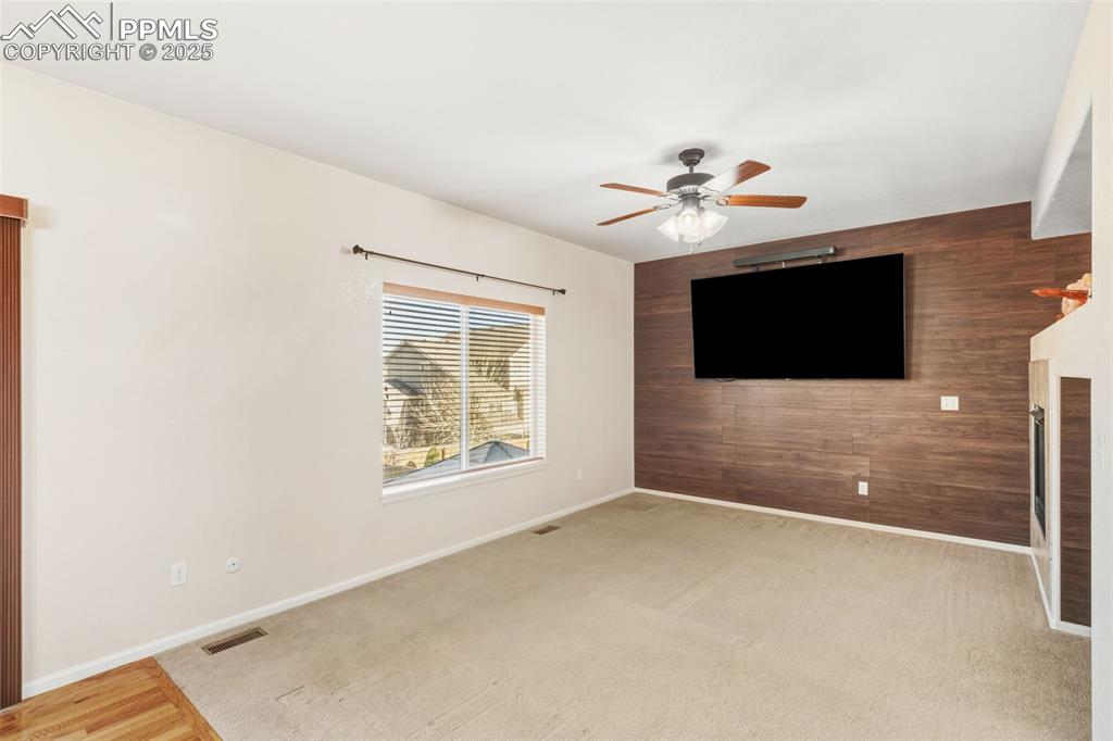 Unfurnished living room featuring wood walls, an accent wall, light carpet, and a ceiling fan