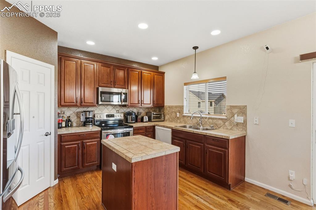 Kitchen with a center island, hanging light fixtures, appliances with stainless steel finishes, light wood finished floors, and brown cabinets