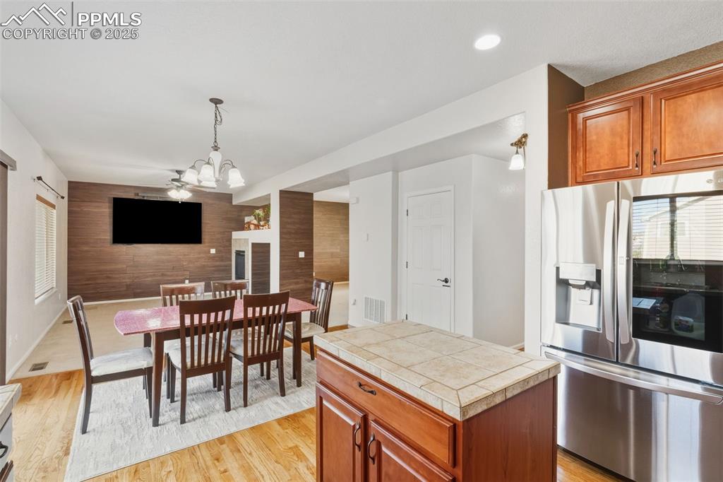 Kitchen featuring an accent wall, stainless steel fridge, brown cabinetry, wood walls, and pendant lighting