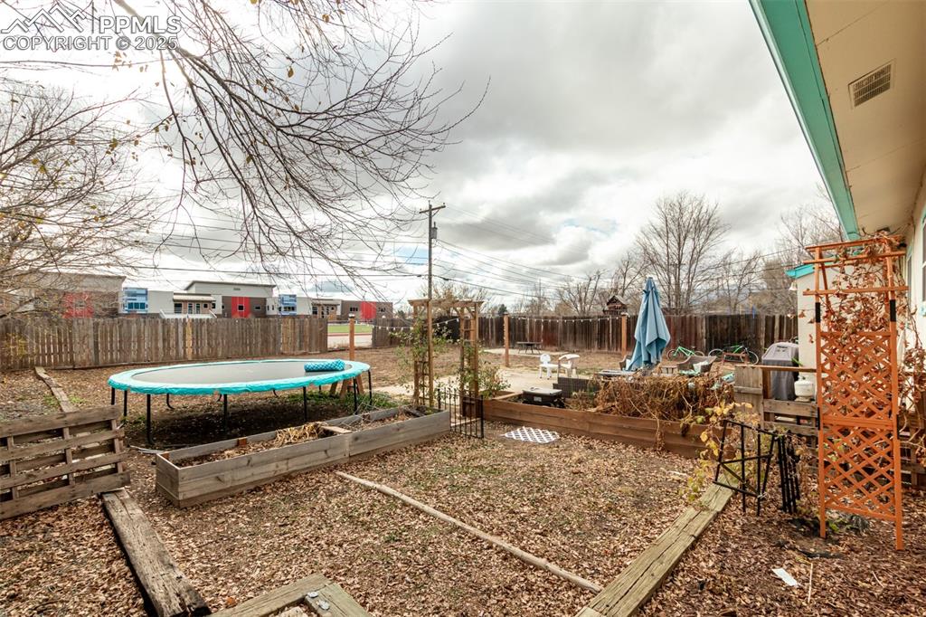 Fenced backyard featuring a garden, a trampoline, and a wooden deck