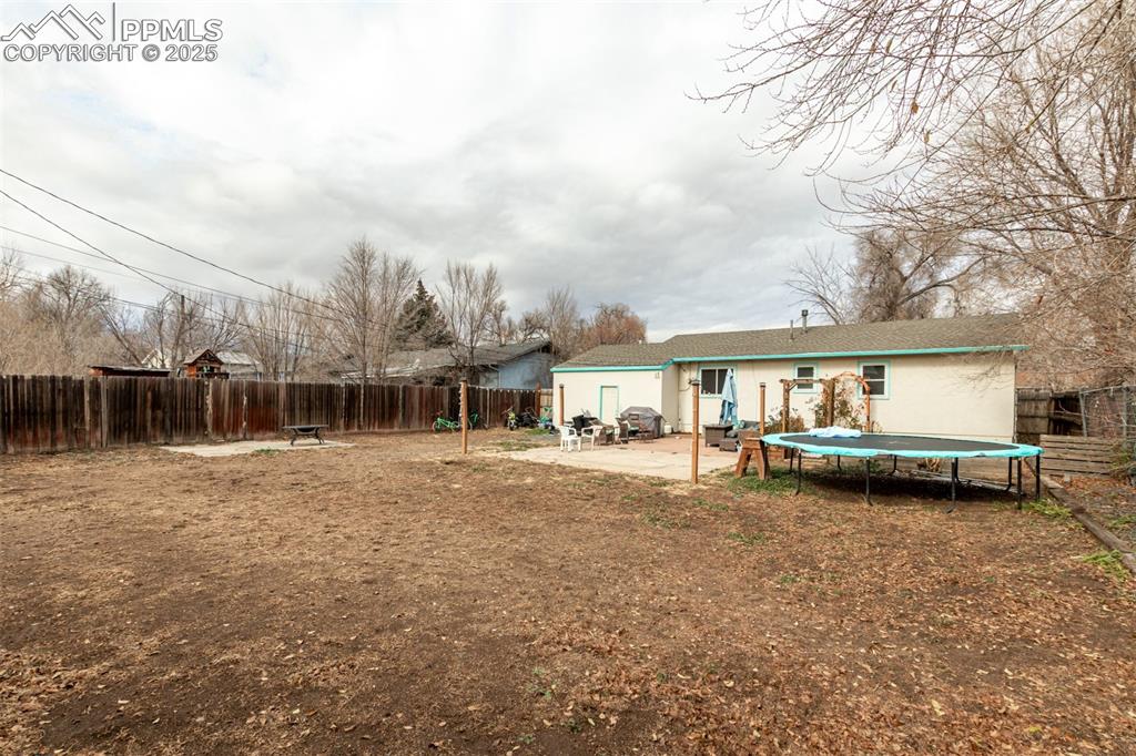 Rear view of house featuring a trampoline, a fenced backyard, and a patio area