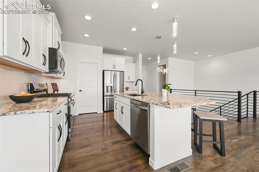 Kitchen with stainless steel appliances, dark wood-type flooring, decorative backsplash, recessed lighting, and a kitchen bar