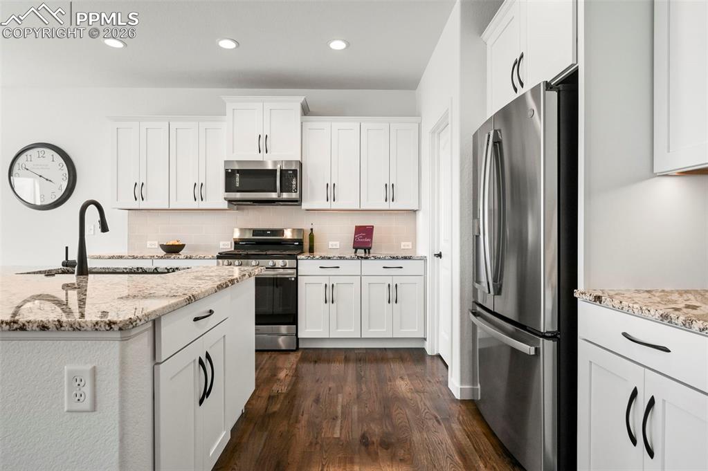 Kitchen with stainless steel appliances, dark wood-style flooring, tasteful backsplash, white cabinetry, and recessed lighting