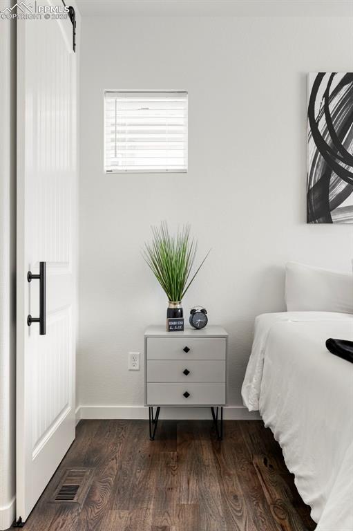 Bedroom with dark wood-style flooring and a barn door