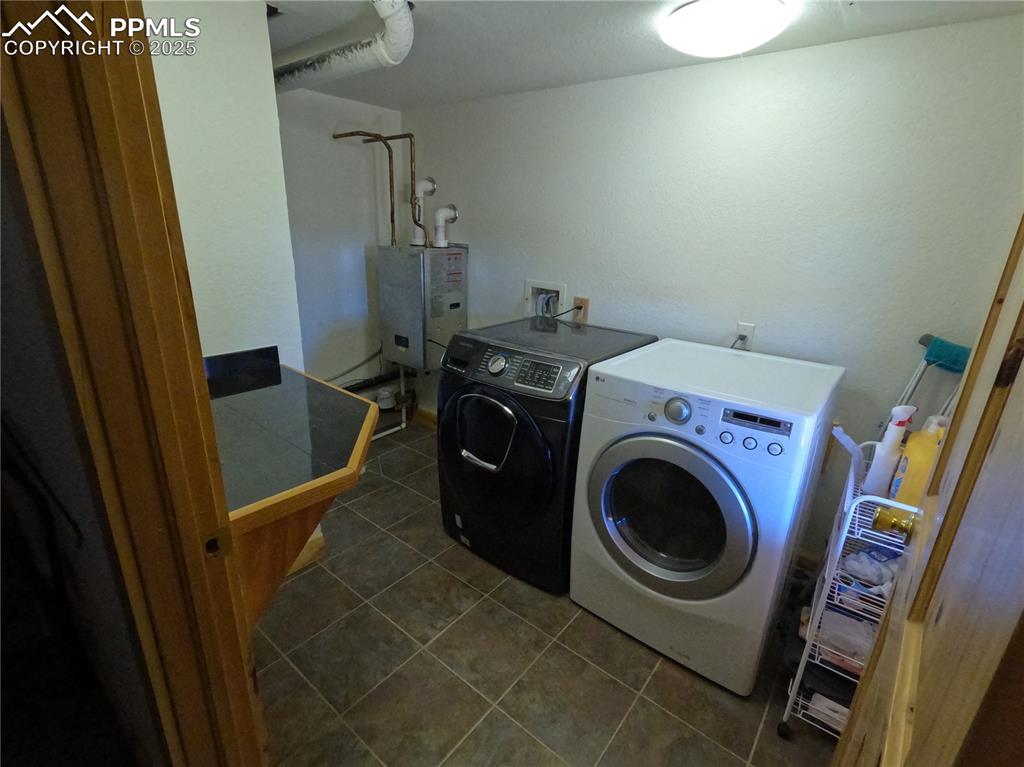 Laundry area featuring dark tile patterned floors, washing machine and clothes dryer, and water heater