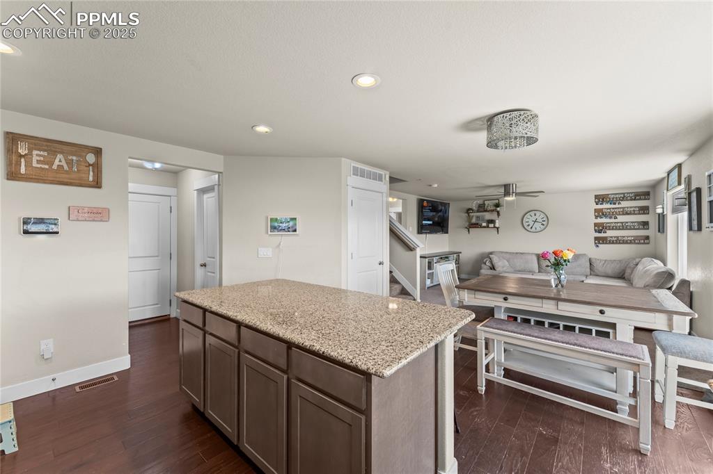 Kitchen featuring a kitchen island, light stone counters, recessed lighting, dark wood-type flooring, and open floor plan