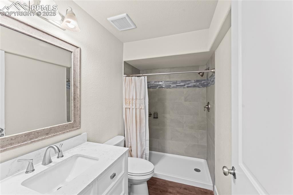 Full bathroom with vanity, dark wood-type flooring, a shower stall, and a textured wall