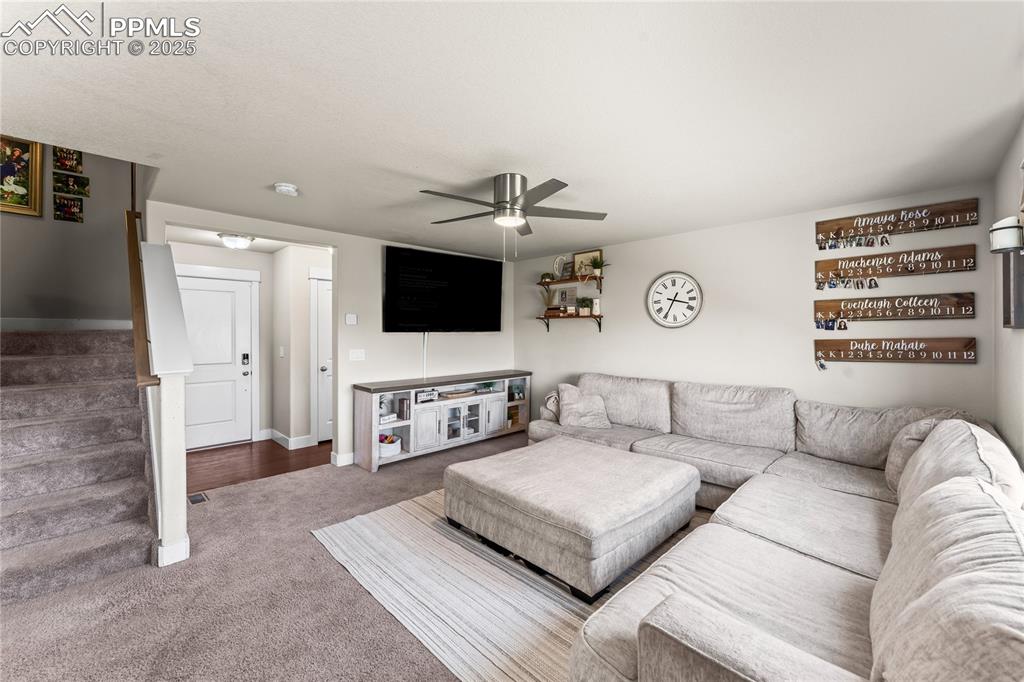 Carpeted living room with stairway and a ceiling fan