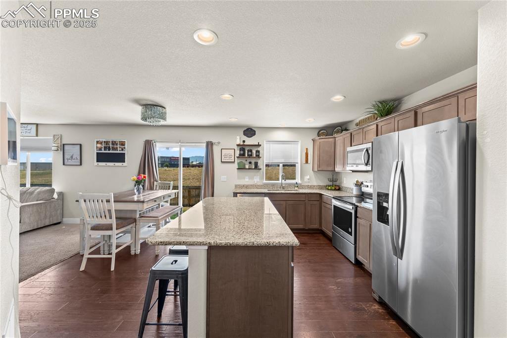 Kitchen featuring stainless steel appliances, light stone countertops, a kitchen island, open shelves, and a kitchen breakfast bar