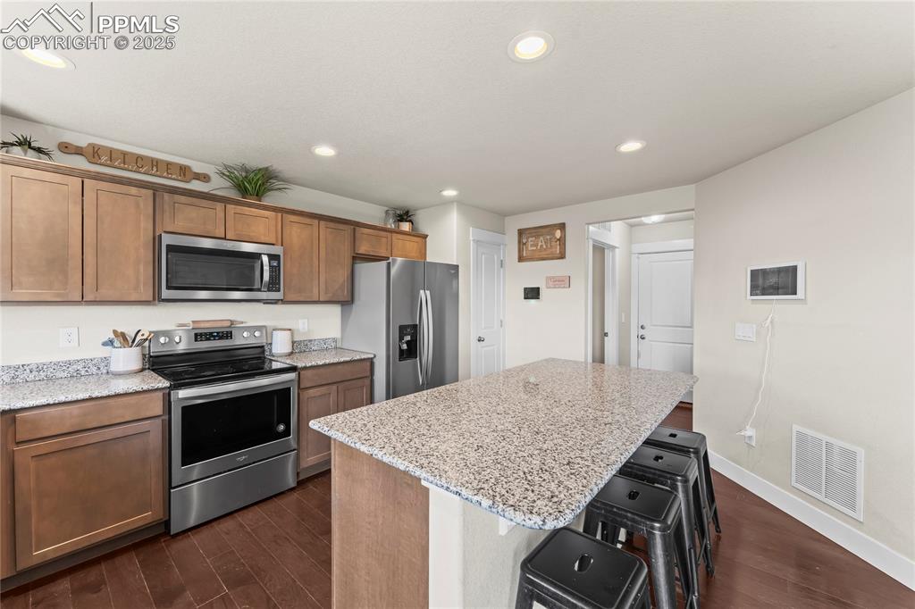 Kitchen featuring appliances with stainless steel finishes, recessed lighting, dark wood-style floors, a center island, and brown cabinetry
