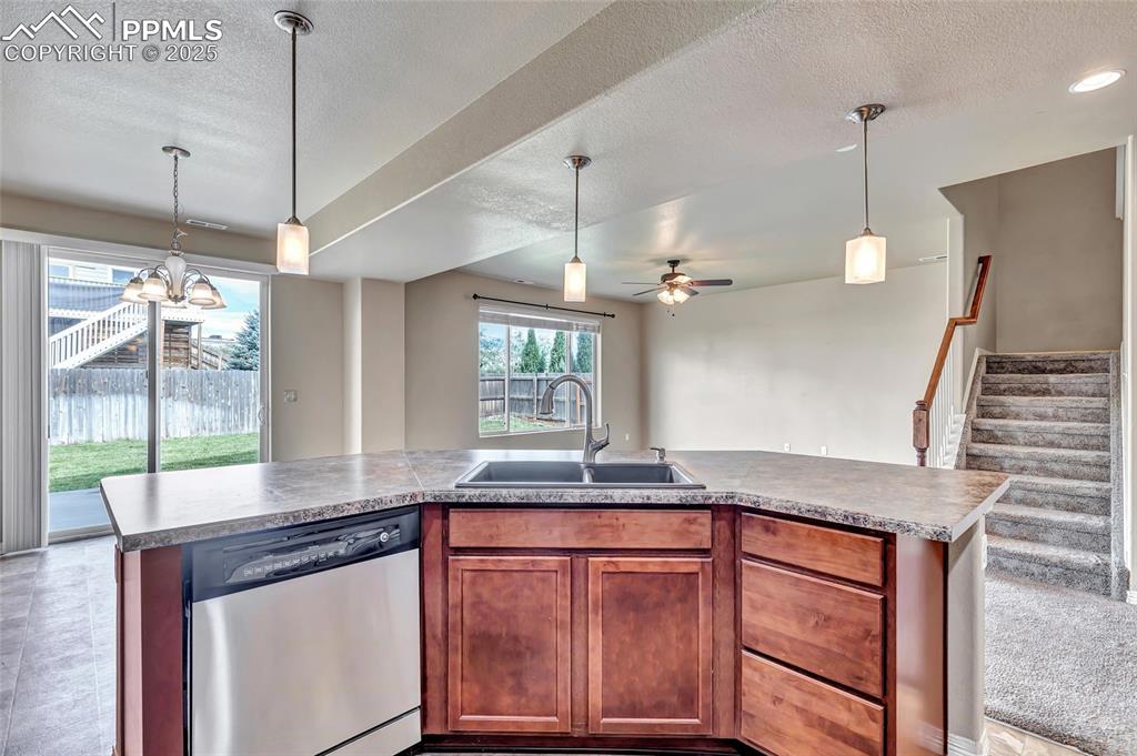 Kitchen with stainless steel dishwasher, hanging light fixtures, brown cabinetry, open floor plan, and a textured ceiling